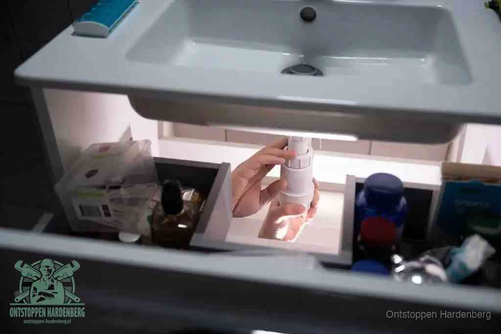 Een pompfles met zeep boven een wastafel, de heet water en afwasmiddel-methode om een vetprop in de afvoer los te maken in Hardenberg