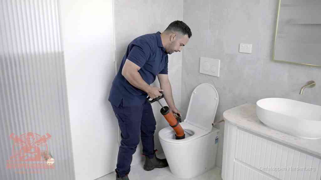 Een monteur buigt over een wandcloset en duwt met de hand een persluchtontstopper in de toiletpot om de verstopping handmatig los te maken in Hardenberg