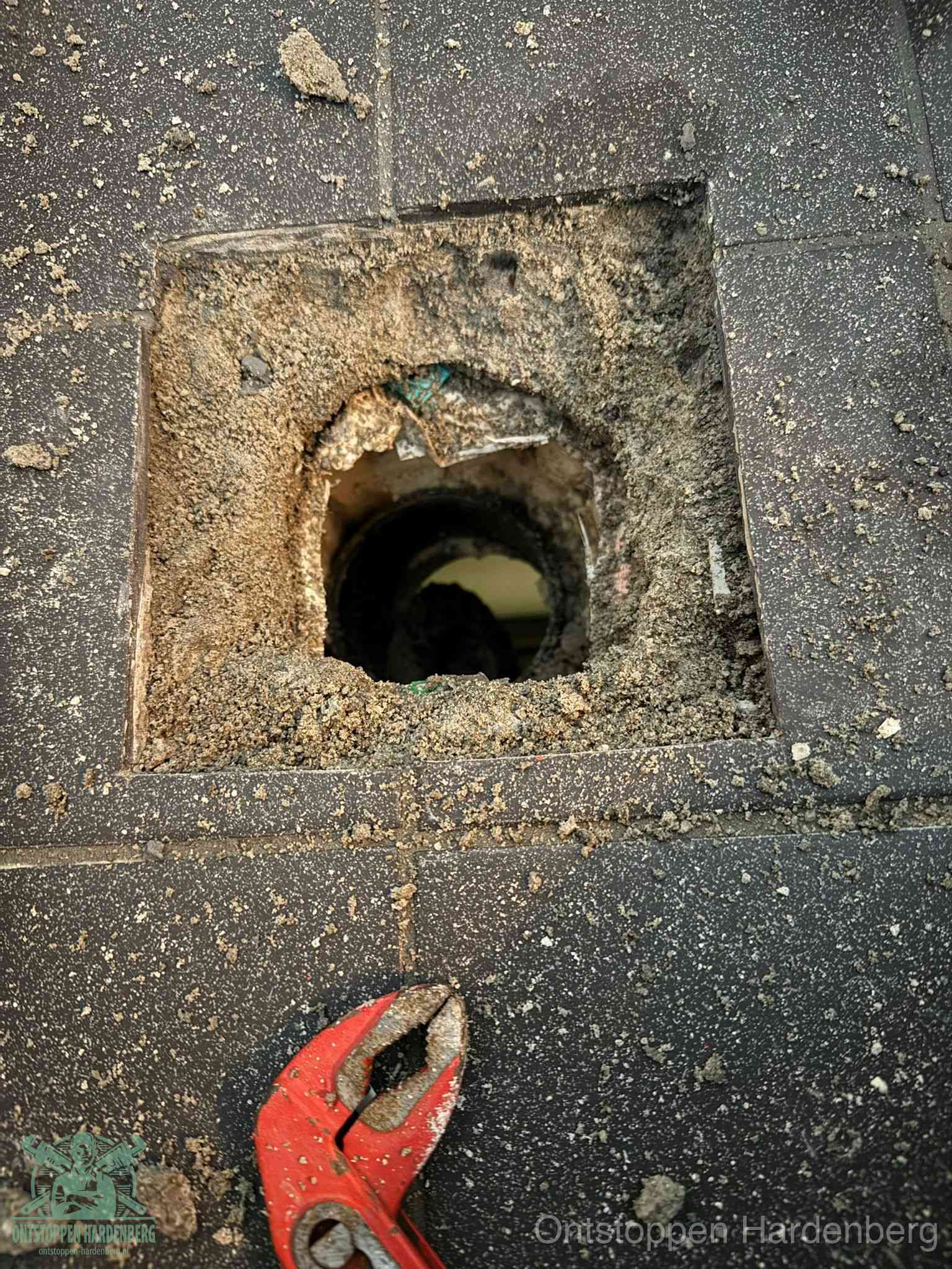 Een geopend rioolputje in een betontegelvloer met losgemaakt rooster en een zichtbare ronde afvoerbuis, het achterhalen waar de afvoerverstopping zit in Hardenberg