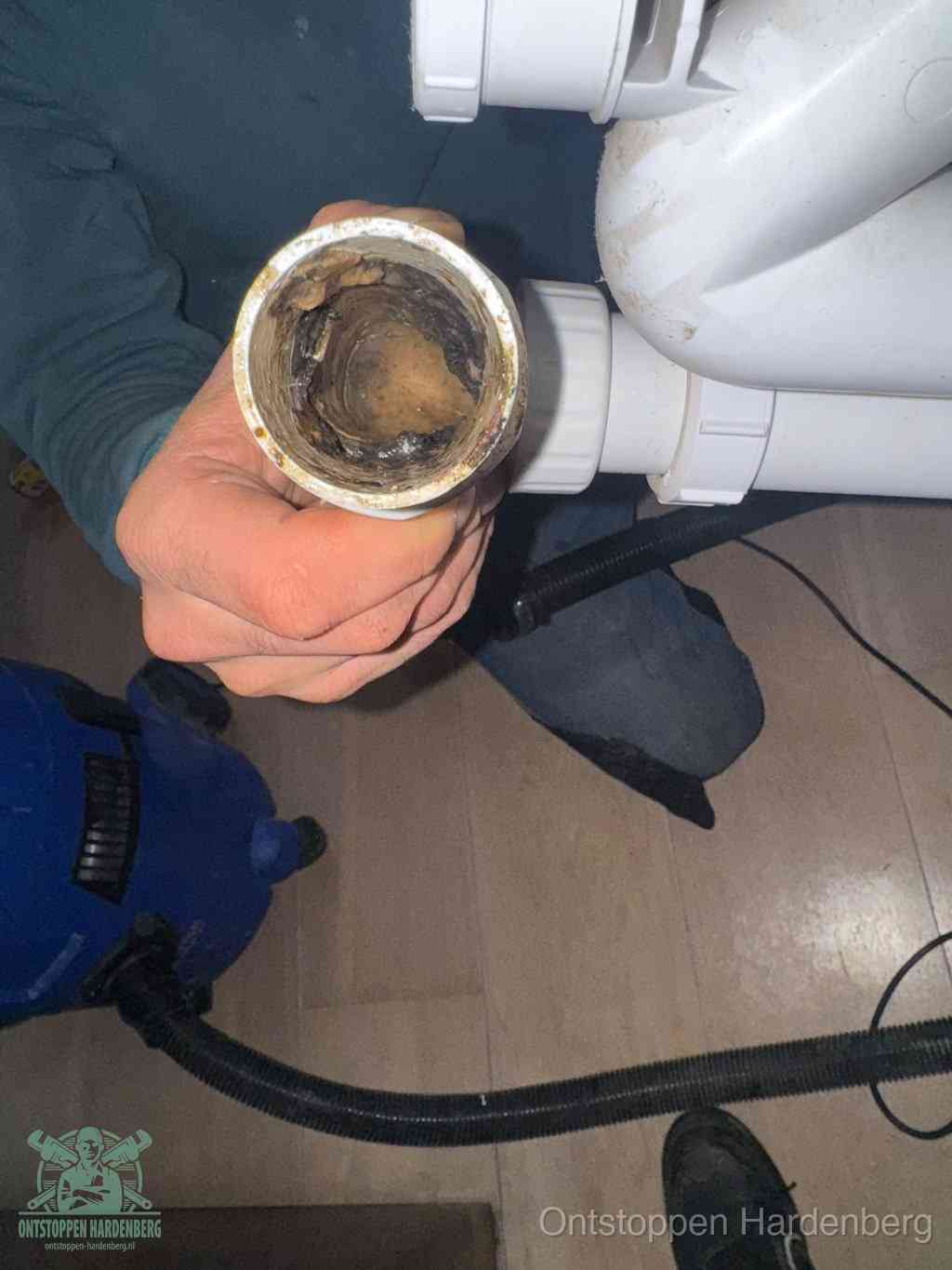Een hand houdt een losgekoppeld PVC-afvoerbuisstuk vast dat van binnen volledig is dichtgeslibd met vet, vuil en aanslag, de meest voorkomende oorzaak van een verstopte afvoer in Hardenberg