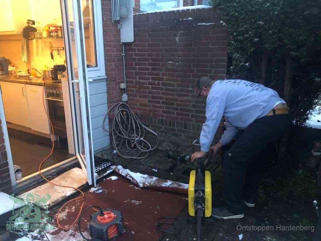 Een monteur werkt buiten bij een open riool-/grondput met een elektrische ontstoppingsmachine om een verborgen afvoerprobleem op te sporen in Hardenberg