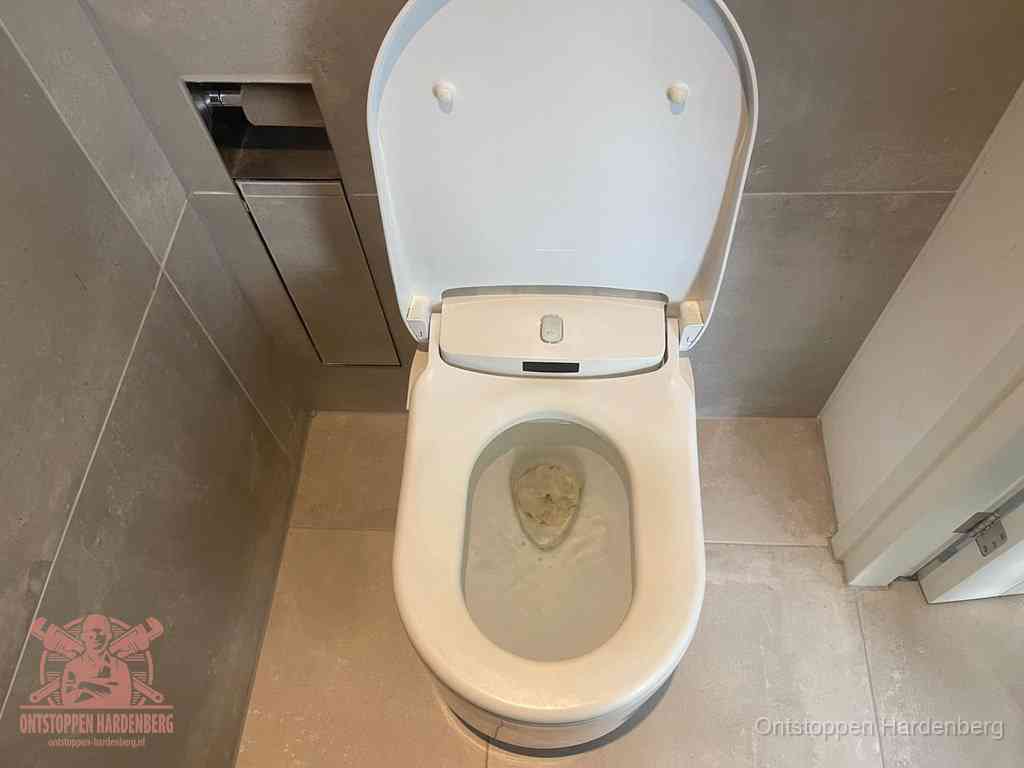 Een wit hangtoilet waarin een prop wc-papier op het water blijft drijven, een duidelijk signaal van een verstopte wc in Hardenberg