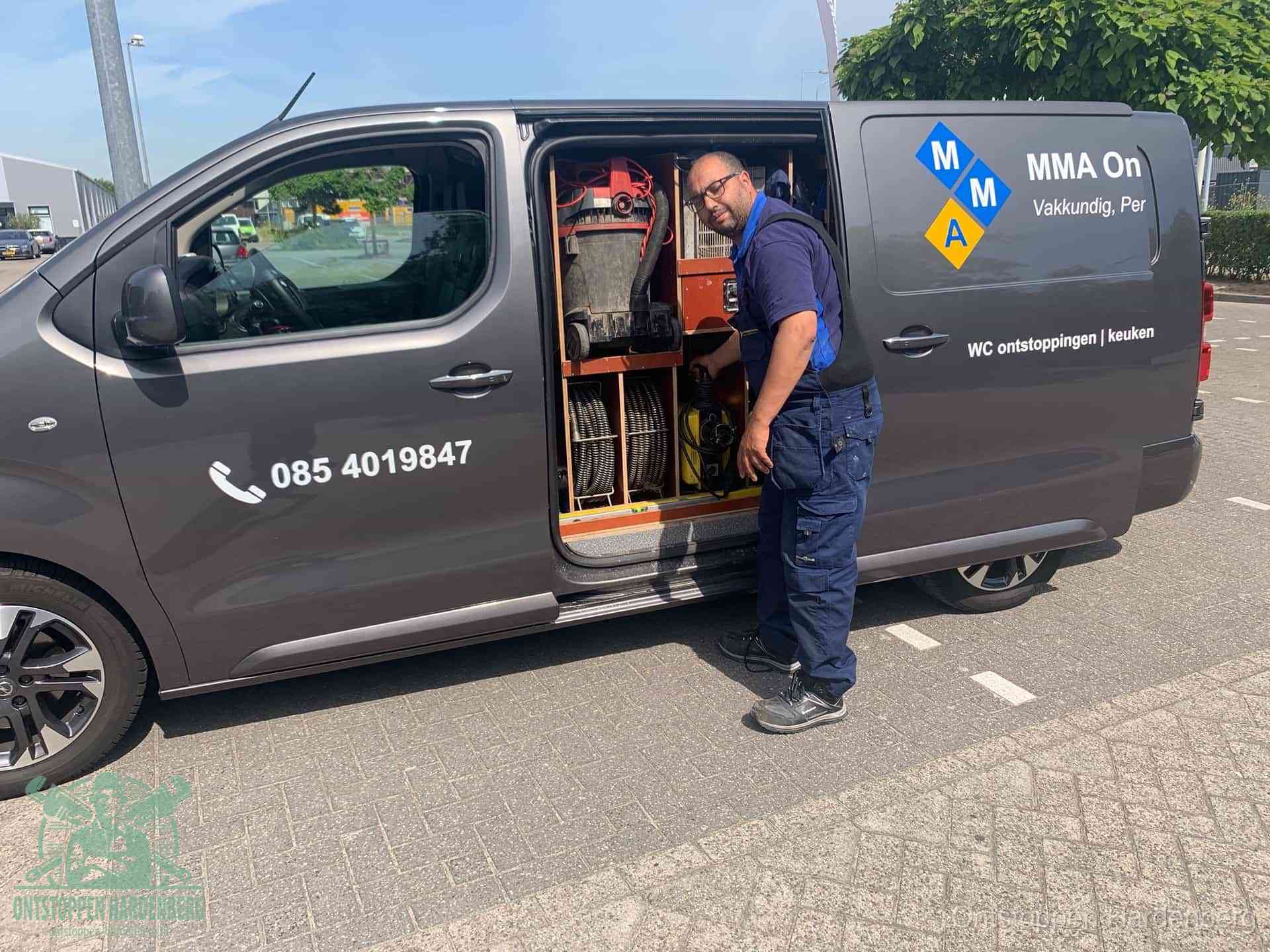 Een monteur bij de open schuifdeur van zijn bedrijfsbus op een parkeerplaats, klaar om de oorzaak van terugkerende afvoerverstoppingen aan te pakken in Hardenberg