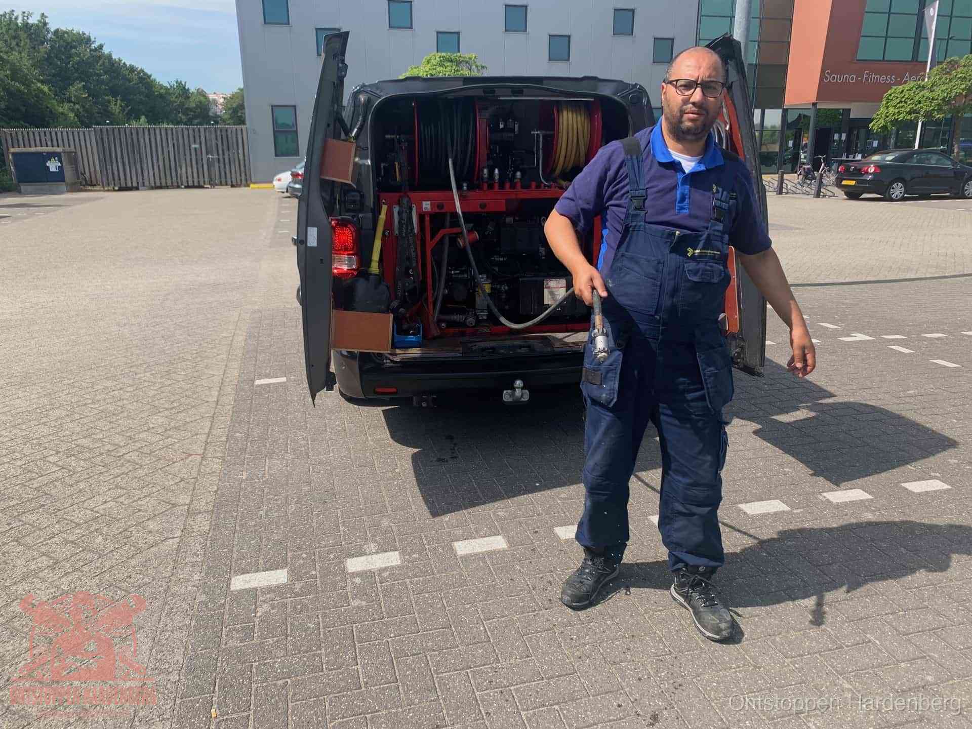 Een monteur bij zijn bestelbus met een hogedruk- en rioolreinigingsunit, klaar om de oorzaak van terugkerende wc-verstoppingen aan te pakken in Hardenberg