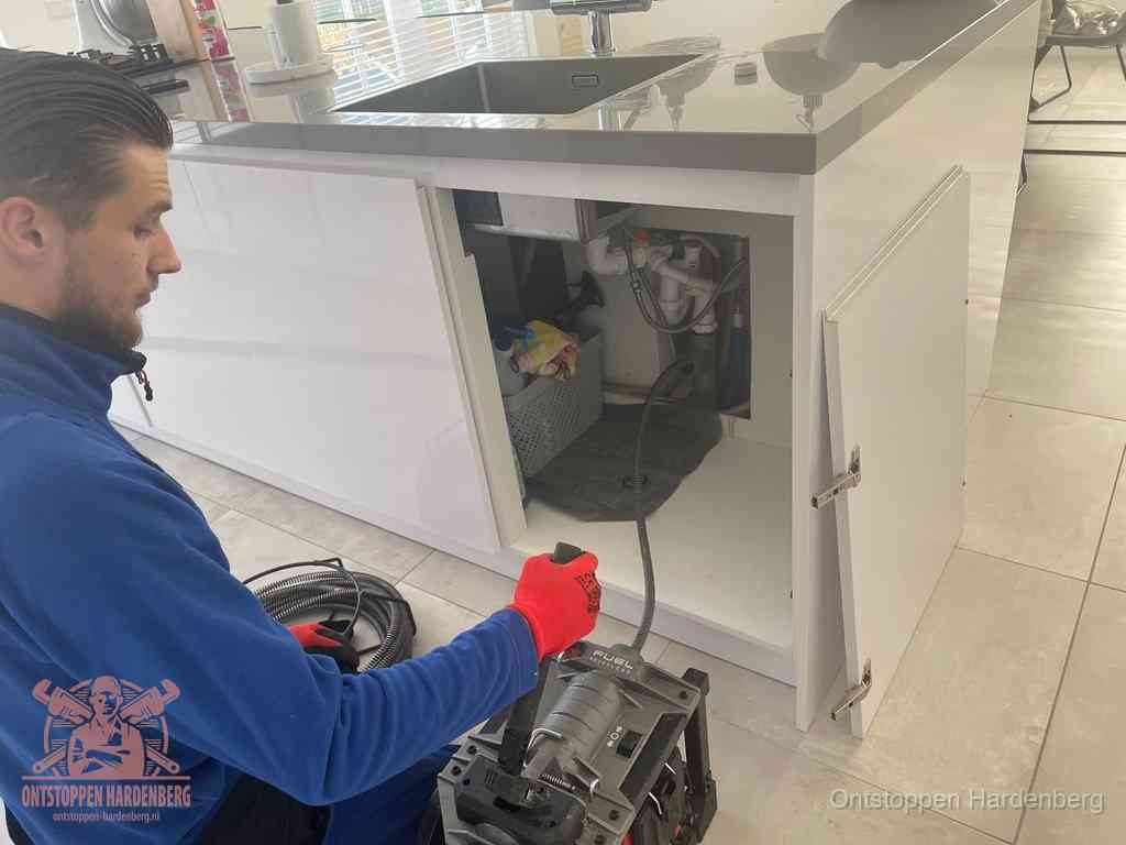 Monteur ontstopt met een veermachine een verstopte afvoer onder de gootsteen in Hardenberg