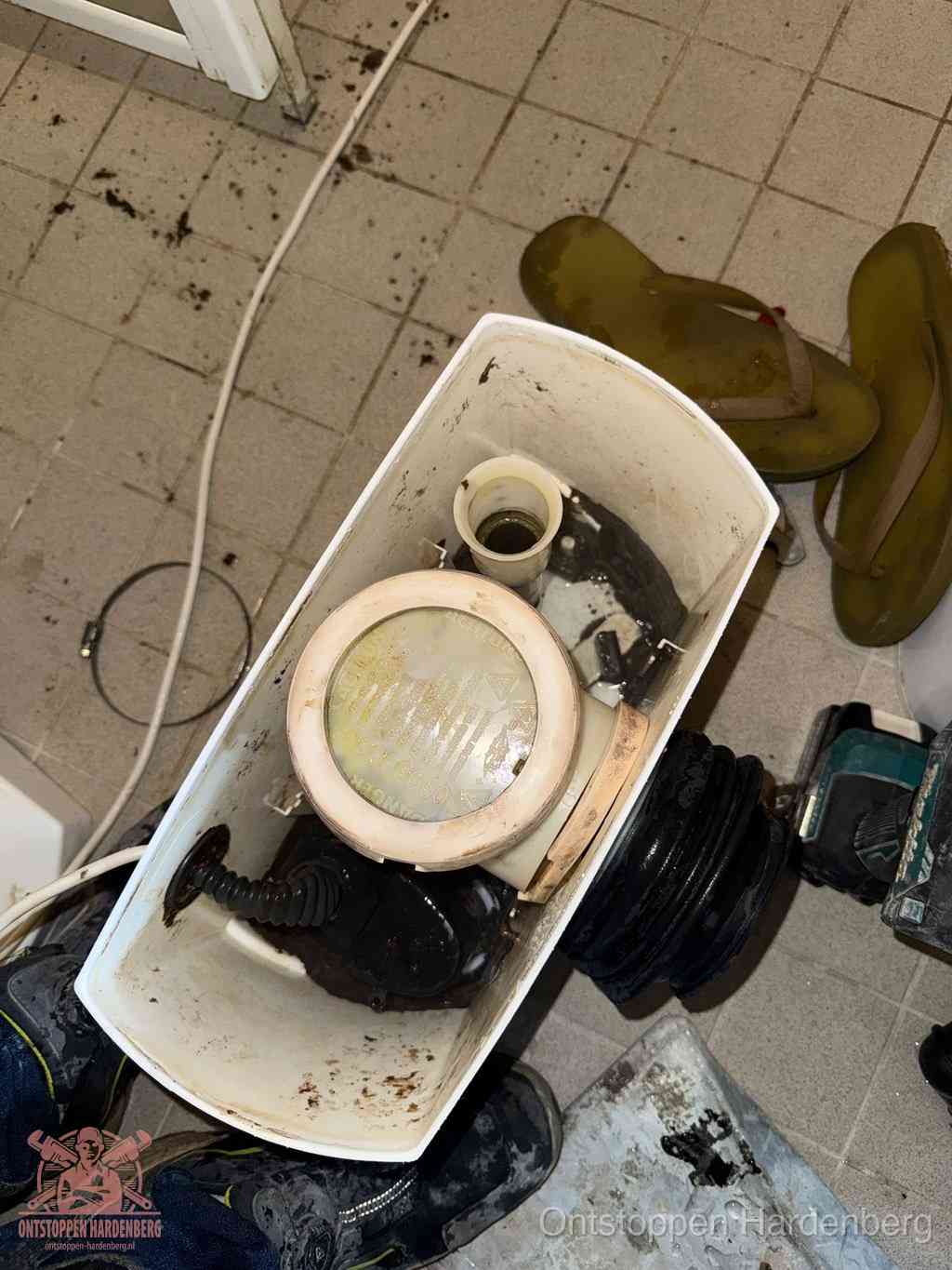 Een gedemonteerde toiletpot op de vloer met ontstoppingsveer en gereedschap ernaast, het verwijderen van een vastzittend voorwerp uit de wc in Hardenberg