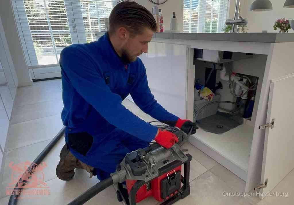 Een monteur voert een professionele elektrische ontstoppingsmachine in de afvoer onder de spoelbak tijdens het gootsteen ontstoppen in Hardenberg