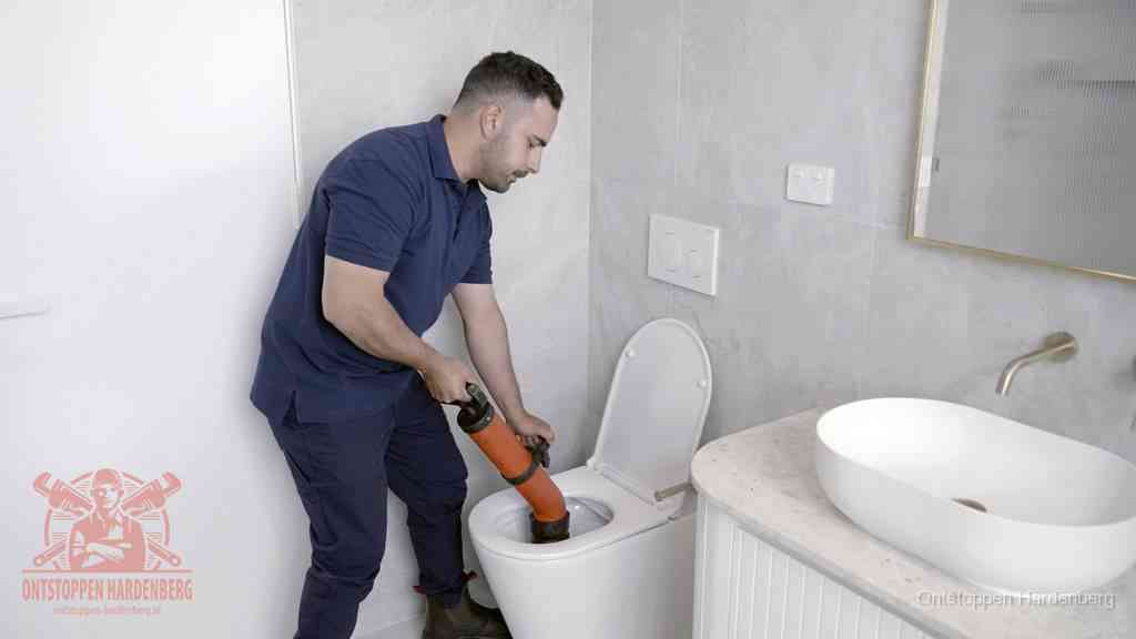 Een man gebruikt een handmatige luchtdruk-ontstopper in een modern betegeld toilet om zelf de wc te ontstoppen in Hardenberg
